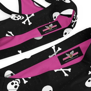 May include: Black and pink bikini with a skull and crossbones pattern. The bikini top has adjustable straps and a racerback style. The bikini bottom has a high-cut leg. The bikini is decorated with a moose logo and the text "Moose Disco" and "www.moosedisco.co.uk".