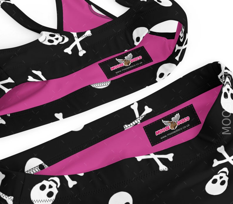 May include: Black and pink bikini with a skull and crossbones pattern. The bikini top has adjustable straps and a racerback style. The bikini bottom has a high-cut leg. The bikini is decorated with a moose logo and the text "Moose Disco" and "www.moosedisco.co.uk".