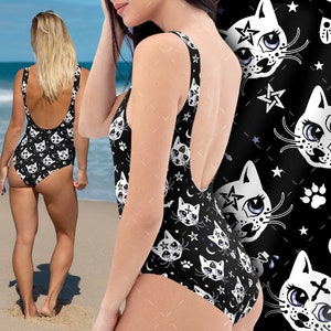 Op de afbeelding: Zwarte badpak met een witte kattenprint. Het kattenontwerp heeft een derde oog en een pentagram. Het badpak heeft een ronde hals en een lage rug.