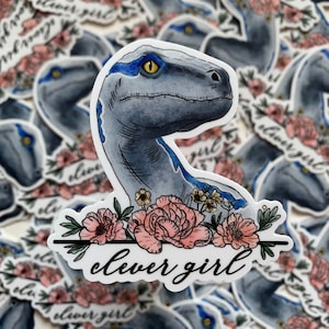 May include: A blue dinosaur sticker with pink flowers and the text "clever girl" on a white background.