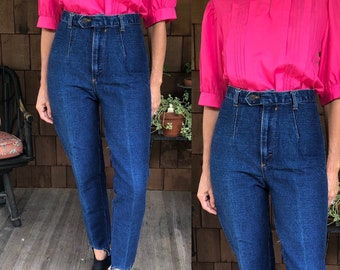 Puede incluir: Un par de pantalones vaqueros de mezclilla azul de cintura alta con pierna recta. Los pantalones tienen cierre de botón y trabillas para cinturón.
