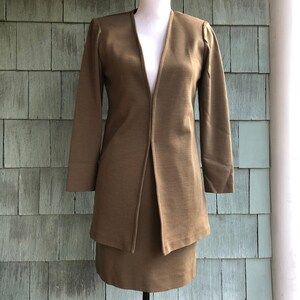 May include: A brown skirt suit with a deep V-neckline and long sleeves. The suit is made of a textured fabric and has a fitted silhouette.