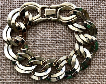 May include: A gold-toned chain link bracelet with a clasp closure. The bracelet features large, interlocking oval links. The clasp is marked with the brand name "Monet". The bracelet is displayed on a textured, neutral-toned surface.