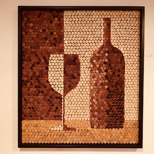 May include: A framed wall art piece made of wine corks, depicting a wine bottle and a wine glass. The corks are arranged in a mosaic pattern, creating a unique and textured design.