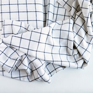 Pu&ograve; includere: Tessuto bianco con motivo a griglia blu navy. Il tessuto &egrave; piegato e drappeggiato, mostrando la trama e il design. Il motivo &egrave; un classico a quadri, adatto a vari progetti di arredamento o abbigliamento.