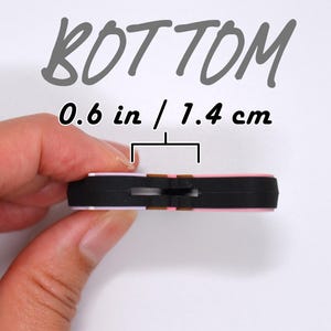 May include: A small, rectangular object with a black base and pink top, measuring 0.6 inches (1.4 cm) across. The word "BOTTOM" is written in a handwritten style above the object.