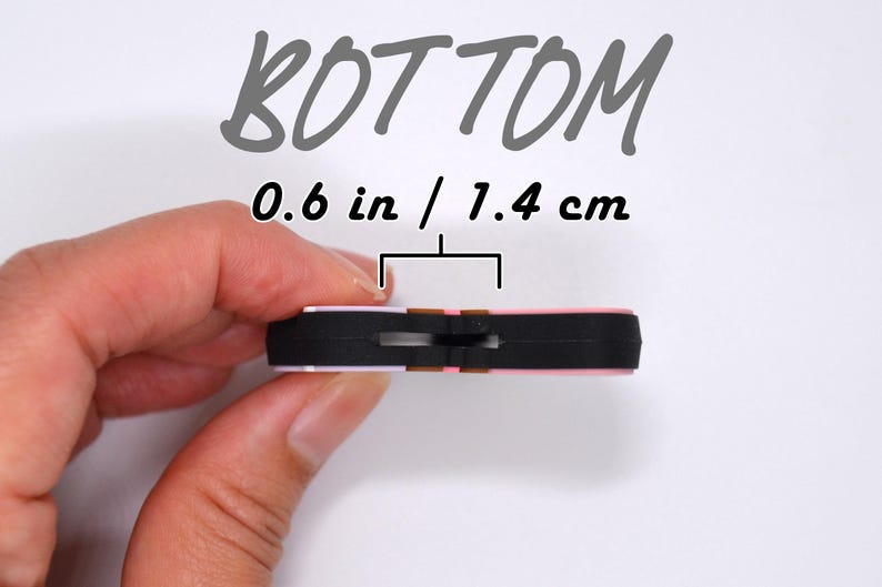 May include: A small, rectangular object with a black base and pink top, measuring 0.6 inches (1.4 cm) across. The word "BOTTOM" is written in a handwritten style above the object.