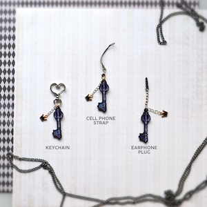 May include: Three key-shaped charms with gold accents and a purple and blue design. The charms are attached to different chains: a keychain, a cell phone strap, and an earphone plug.