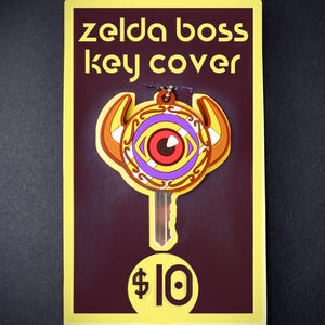 May include: A yellow and brown key cover with a purple and gold eye design. The text "Zelda boss key cover" and "$10" are printed on the card.