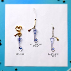 May include: Three keychains featuring a blue and white keyblade design. The keychains are displayed on a white background with the words "KEYCHAIN", "CELL PHONE STRAP", and "EARPHONE PLUG" printed below each keychain.