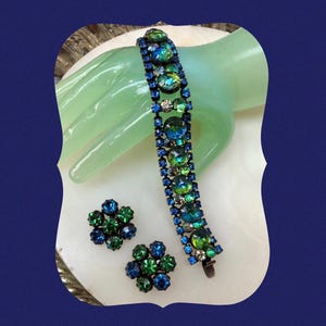 Könnte beinhalten: Ein Vintage-Armband und Ohrring-Set mit einem abgestuften Design aus blauen und grünen Strasssteinen. Das Armband ist aus Metall und hat einen Verschluss. Die Ohrringe sind im Clip-Stil.