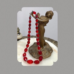 May include: A red glass bead necklace with a silver clasp. The necklace is draped over a decorative stand.