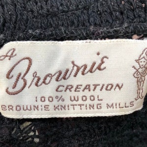 May include: A white label with brown text that reads "A Brownie Creation 100% Wool Brownie Knitting Mills". A cartoon illustration of a person holding a musical instrument is on the right side of the label.