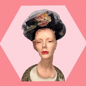 Puede incluir: Un sombrero negro con velo y flores rosas y blancas. El sombrero está en la cabeza de un maniquí.