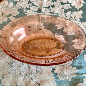 May include: A pink glass serving bowl with a floral design. The bowl has a scalloped edge and is made of clear glass with a pink tint.
