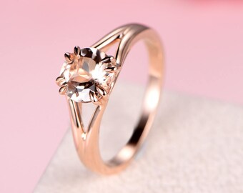 May include: A rose gold ring with a clear oval-shaped gemstone set in a prong setting. The ring has a delicate, open-work design.