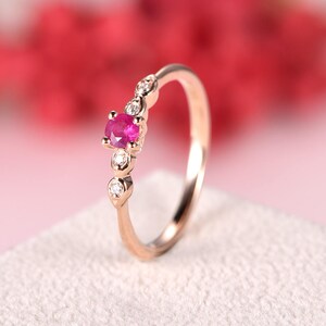 Op de afbeelding: Een delicate ring van roségoud met een enkele roze robijn, omringd door kleinere diamanten. De ring ligt op een witte achtergrond.