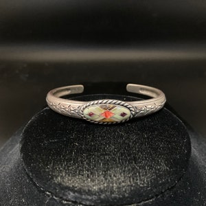 May include: A silver bracelet with a colourful inlay of stones in an oval shape. The bracelet has a floral design on the band.