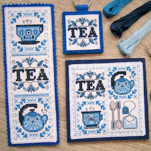 May include: Three cross-stitch embroidery patterns with blue and white thread on white fabric. The patterns feature the word "TEA" and images of teacups and teapots. The patterns are mounted on blue felt.