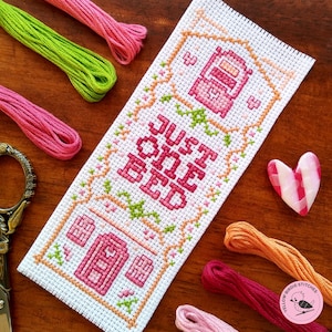 May include: Cross stitch pattern with a pink and green design. The pattern says "Just one bed".