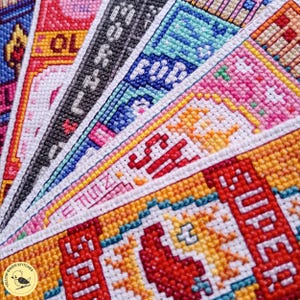May include: A collection of colorful cross-stitch fabric strips arranged in a fan pattern. The embroidery features vibrant pixelated designs in shades of red, orange, yellow, blue, pink, and black, with visible text including SUPER, SH, and MORNING.
