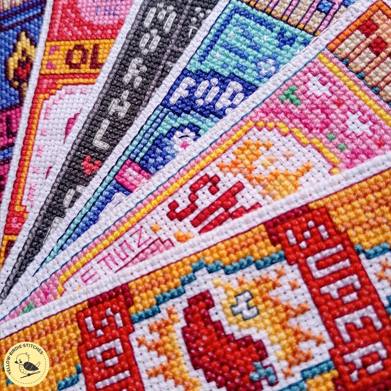 May include: A collection of colorful cross-stitch fabric strips arranged in a fan pattern. The embroidery features vibrant pixelated designs in shades of red, orange, yellow, blue, pink, and black, with visible text including SUPER, SH, and MORNING.