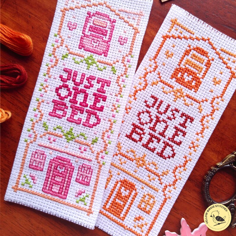 May include: Two cross-stitch bookmarks with a pink and orange color scheme. The bookmarks feature a small house with the text "Just One Bed" on each.