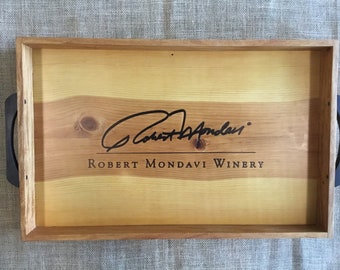 May include: A wooden serving tray with black handles. The tray is engraved with the text "Robert Mondavi Winery" and a signature.
