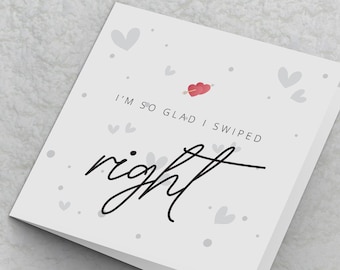 May include: A white card with a red heart and arrow, and the text "I'm so glad I swiped right". The card is decorated with small grey hearts.