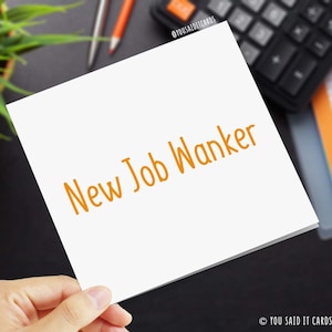 May include: A white card with the text "New Job Wanker" written in orange.