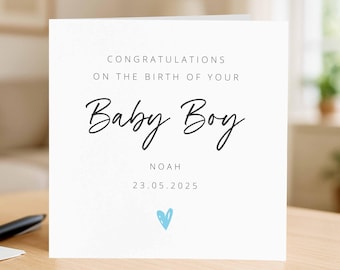 May include: A white card with the text "CONGRATULATIONS ON THE BIRTH OF YOUR Baby Boy" in black script. The name "NOAH" and the date "23.05.2025" are below the text. A small blue heart is at the bottom.