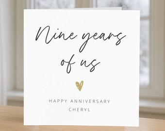 May include: White card with black text that reads "Nine years of us" with a gold heart below. The text "Happy Anniversary Cheryl" is printed below the heart.