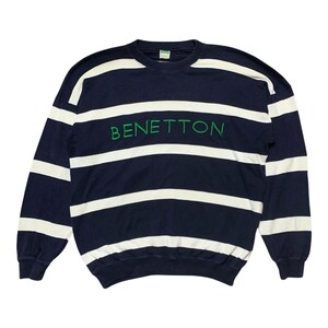 May include: A long-sleeve crewneck sweatshirt featuring horizontal navy blue and white stripes. The word BENETTON is embroidered in green thread across the center of the chest. The garment has a ribbed collar, cuffs, and hemline.
