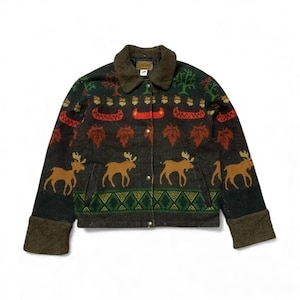 May include: A dark charcoal grey jacket featuring a brown fleece collar and cuffs. The jacket displays a repeating pattern of tan moose, orange maple leaves, red canoes, and green trees, with a geometric green and yellow border at the hem.