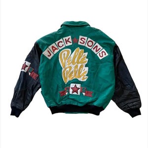 May include: A green and black leather jacket featuring the text JACK SONS in red letters and Pelle Pelle in yellow script on the back. The design includes red star appliques, a black ribbed hem and cuffs, and a collar. The sleeves are black leather.