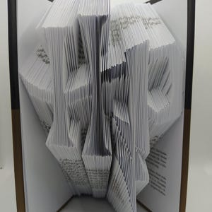 May include: An open book with pages intricately folded to create a three-dimensional sculpture. The book's cover is dark, and the pages are white, forming a geometric design. The text "REDMI NOTE 8T AI QUAD CAMERA" is visible.