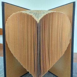 May include: A book with pages folded into a heart shape. The pages are a light brown color, and the edges are slightly uneven. The book's cover is dark blue, and the pages are fanned out to display the heart shape.