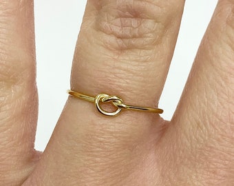 May include: A simple gold knot ring. The ring is thin and delicate, with a small knot in the centre.