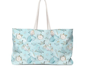 Puede incluir: Una bolsa de lona azul claro con un asa de cuerda blanca. La bolsa presenta un patrón repetido de Cenicienta con su vestido azul, un carruaje, un zapato de cristal y una varita mágica. El fondo es azul claro con purpurina dorada.