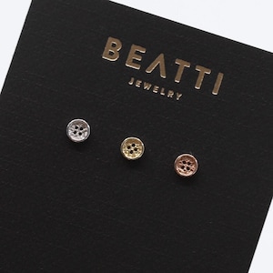 Peut inclure: Trois petites boucles d'oreilles rondes et texturées en argent, or et or rose sur une carte noire avec le texte "BEATTJ JEWELRY" et "BEATTJ.COM".