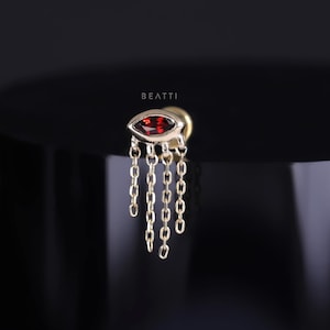 May include: Gold body jewellery featuring a red gemstone in a marquise shape with a dangling chain.