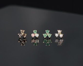 May include: Four gold stud earrings, each featuring a trio of small round gemstones arranged in a clover-like shape. The stones include dark brown, pink and white, green, and clear white varieties, all set in polished gold metal prongs.