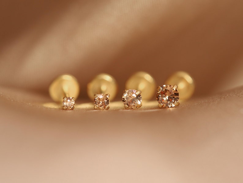 May include: Five gold stud earrings with small, round, champagne-colored gemstones.
