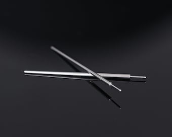 May include: Two silver metal tools with pointed tips are crossed against a dark background. One tool has a small, rounded tip. The tools appear to be precision instruments, possibly for crafting or technical work.