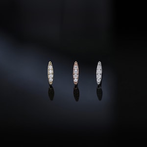 May include: Three stud earrings in gold, rose gold, and silver, each with a row of small, sparkling clear stones. The earrings are oval-shaped and set against a dark, reflective background.
