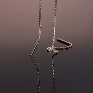 Puede incluir: Un par de pendientes de cadena dorada con una barra larga, delgada y recta que cuelga de cada cadena.