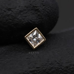 May include: A gold square-shaped earring with a clear square-shaped gemstone in the centre.