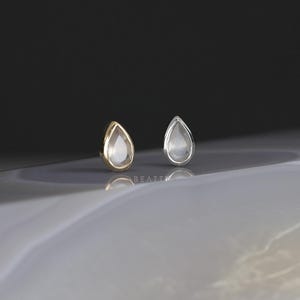 May include: Two teardrop-shaped earrings, one gold and one silver, with clear stones set in the center.
