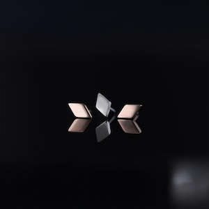 May include: Three diamond-shaped stud earrings. Two are rose gold, and one is silver. The earrings are displayed on a reflective black surface, creating mirrored reflections of each earring. The earrings are minimalist and modern.