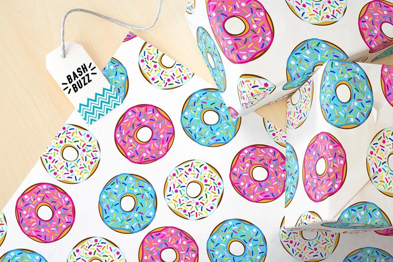K&ouml;nnte beinhalten: Wei&szlig;es Geschenkpapier mit einem sich wiederholenden Muster aus bunten Donuts mit Streuseln. Die Donuts sind rosa, blau und wei&szlig; mit bunten Streuseln.